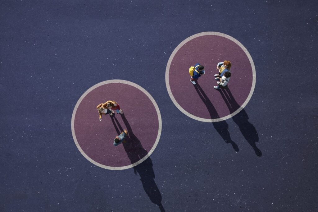 An aerial view of two groups of people standing in separate circles on a dark purple surface, casting long shadows.